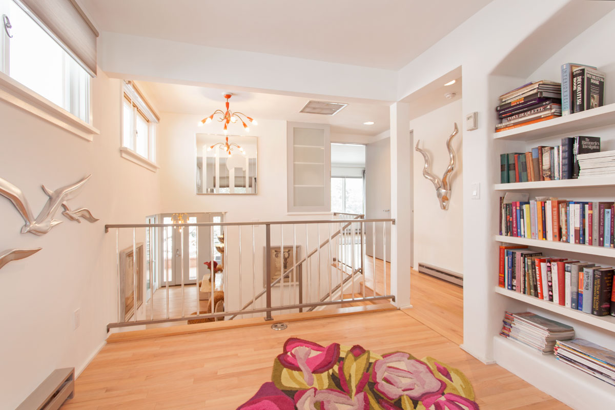The second floor is enhanced by wall-hung solid brass seagull decorations and a vibrant, multicolored modern chandelier. A floral rug lies adjacent to the bookshelf, adding a touch of warmth and charm to the room.
