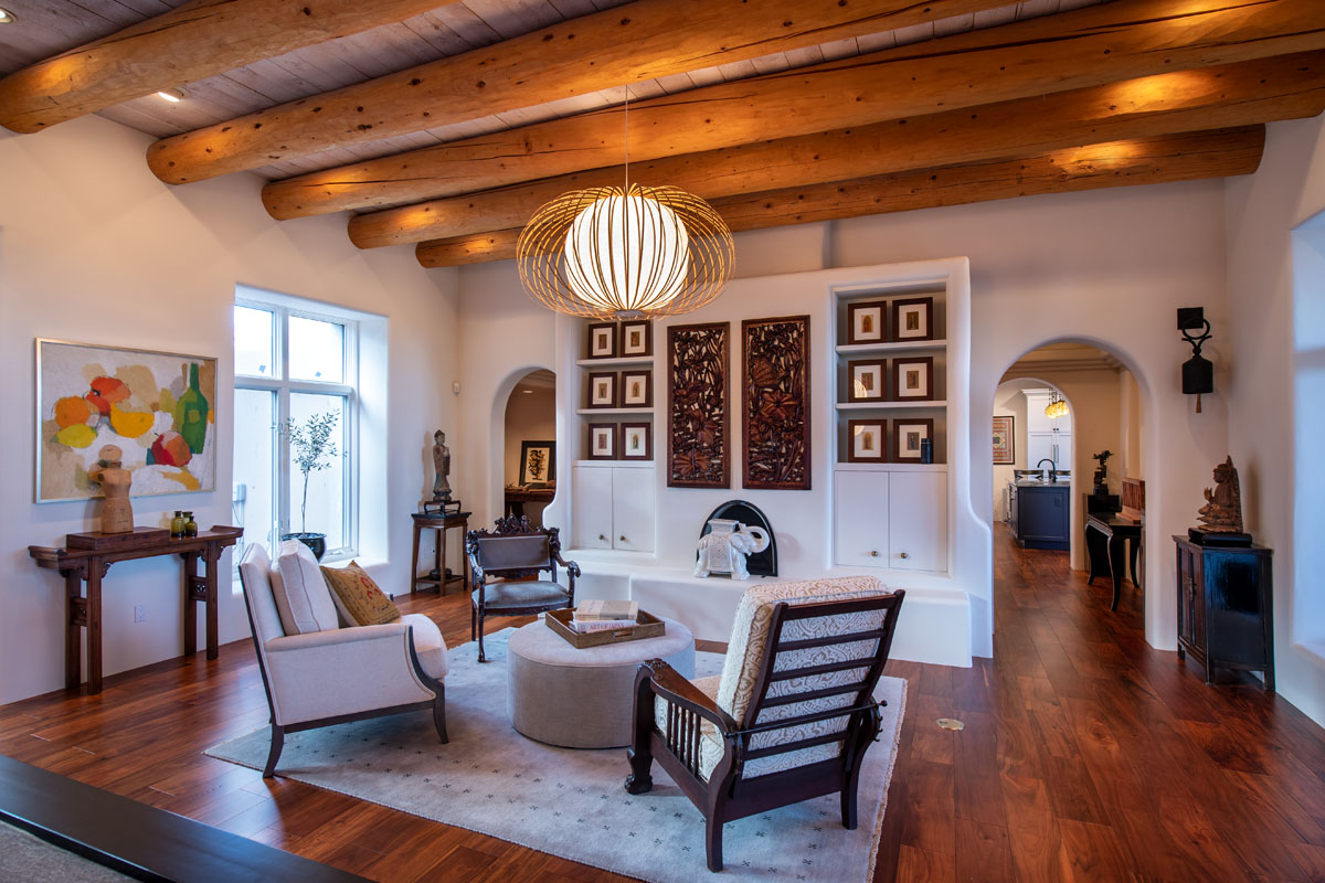 The living room boasts acacia wood floors, a vintage armchair, white carpet, and wooden beams, highlighted by native pendant lights and an art wall with vintage decor.