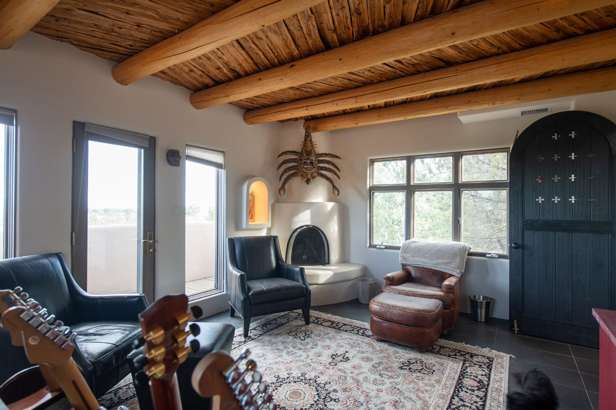 In a home blending Asian design with New Mexico style, the living room features wooden beams, a vintage rug, a leather chair, and a rustic cellar door.