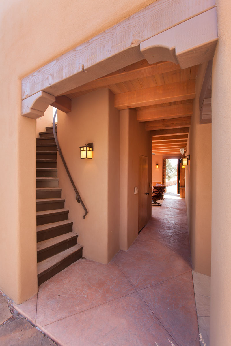 The curbed adobe staircase elegantly transitions to a walkway adorned with blush pink floor tiles. This path, imbued with charm, gracefully leads to the welcoming environment of the living room.