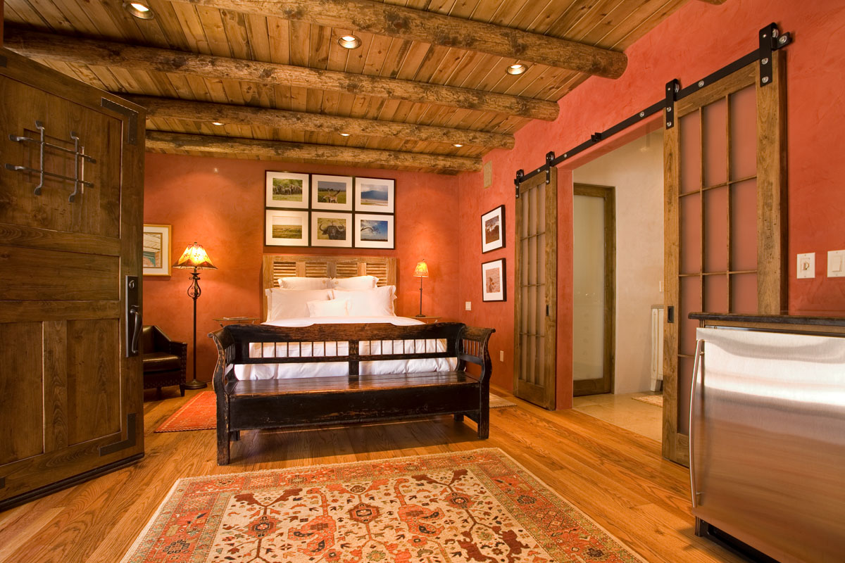 The master bedroom and bathroom renovation, featuring a red southwestern theme, includes wood furniture, a vibrant carpet, and a cozy fireplace. The continuity of the theme is maintained with wood floors and ceilings, enhancing the rustic charm.