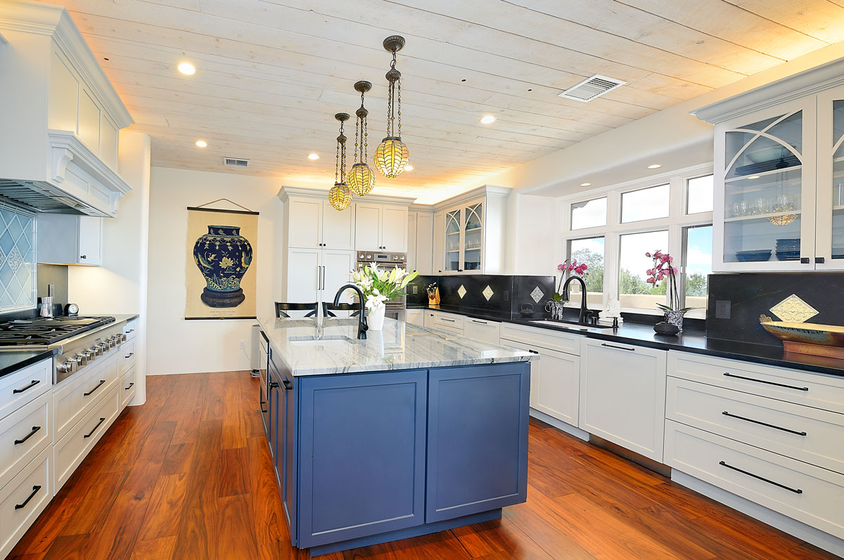 The vintage-inspired kitchen features cobalt blue cabinets with granite countertops, contrasting white cabinets with black tops, hardwood planks, and ambient pendant lights.