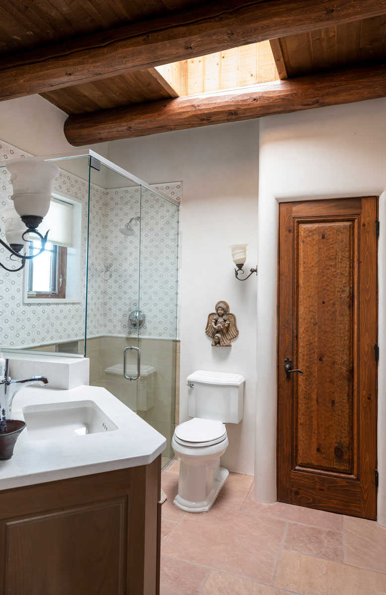 The bathroom combines natural charm and modern design with its flagstone flooring, glass shower space, and wooden ceiling and doors. A skylight adds an airy feel, while a chic wall decoration lends an elegant touch.