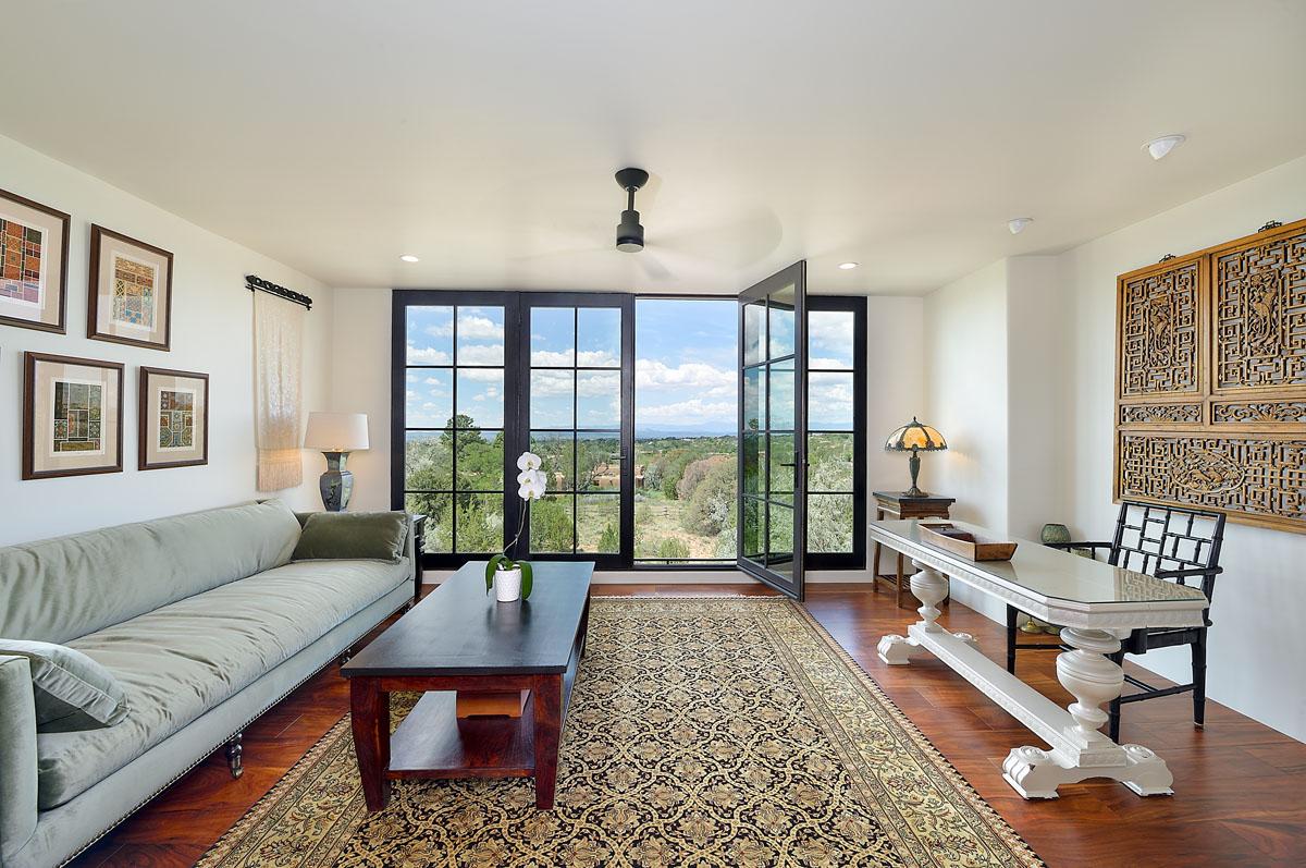 With breathtaking views of the Jemez and Ortiz mountains, the living room features a French upholstered sofa, a vintage rug, French doors, and a handcrafted artisan table.