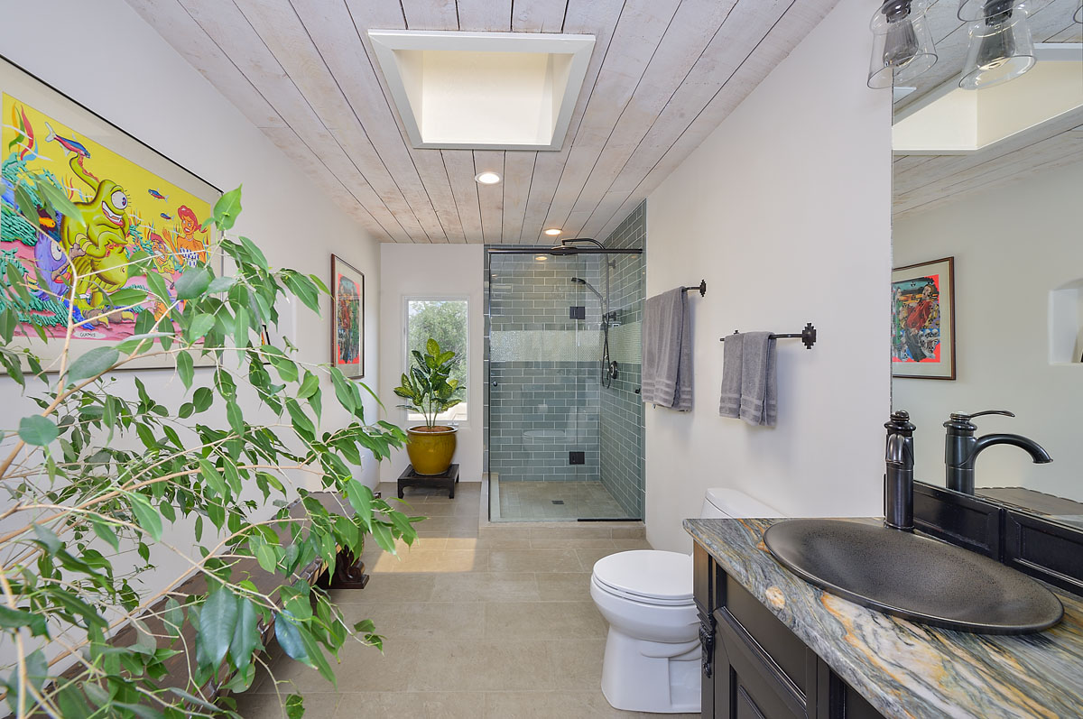 Blending Asian design with New Mexico warmth, the bathroom boasts ficus tree leaves, a copper vessel sink on a marble countertop, and a glass-enclosed shower with marble floor tiles.