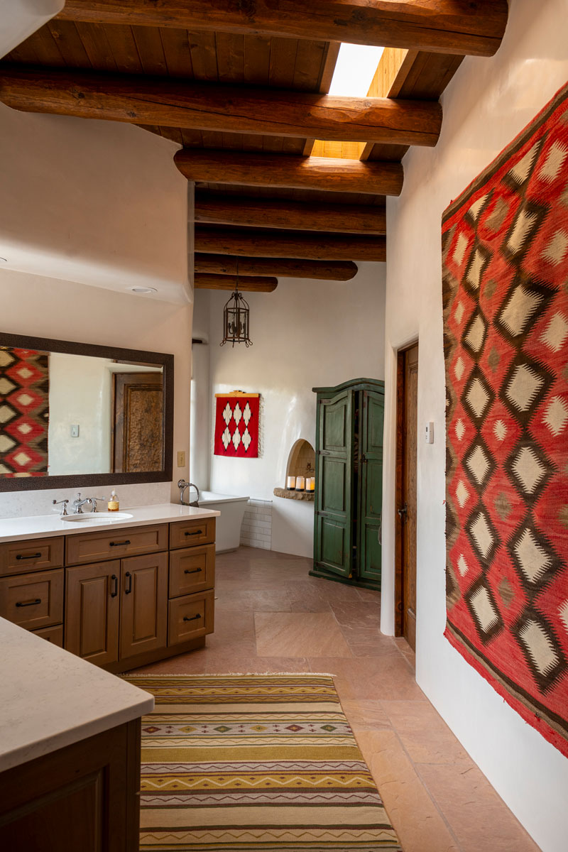 The guest bathroom boasts a lively mix of green, yellow, and red tones. A wall-hung geometric red rug, a Southwest-style yellow print floor rug, a green cabinet, and wooden ceilings come together to create an eccentric touch.