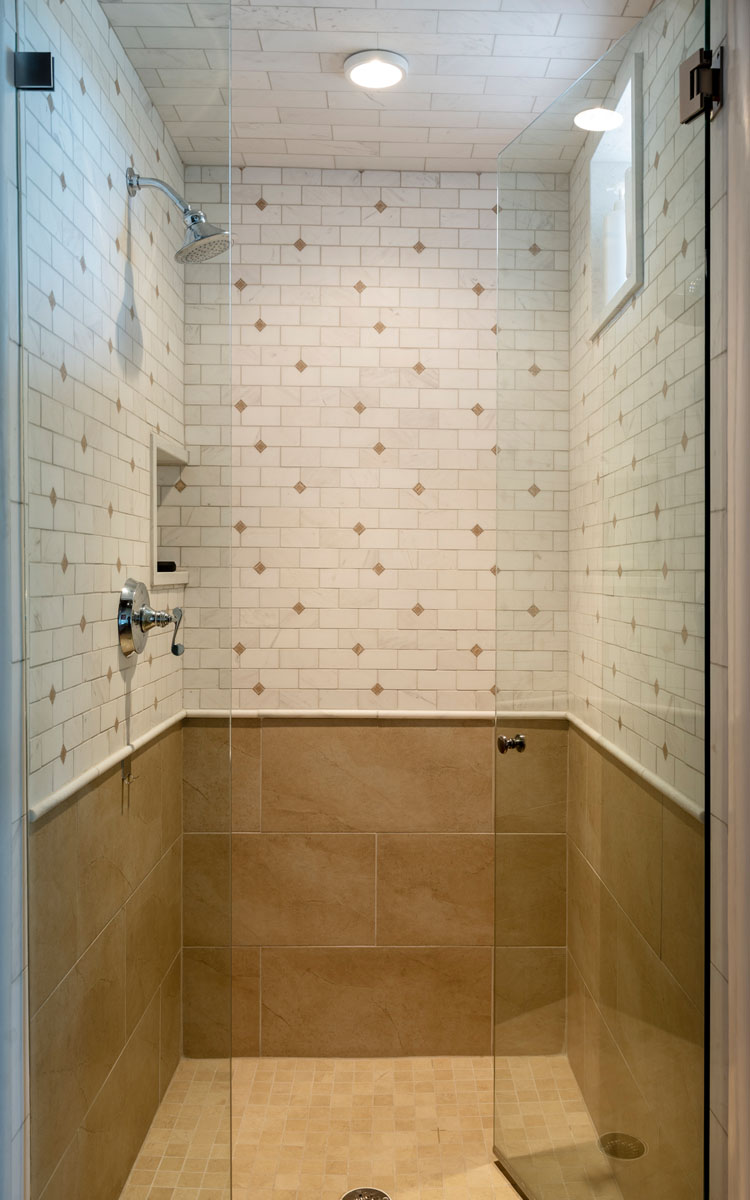 The shower room, with its minimalist design of beige and rusted gold tiles and clear glass doors, is further enhanced by a wooden ceiling, a skylight, and wooden doors.