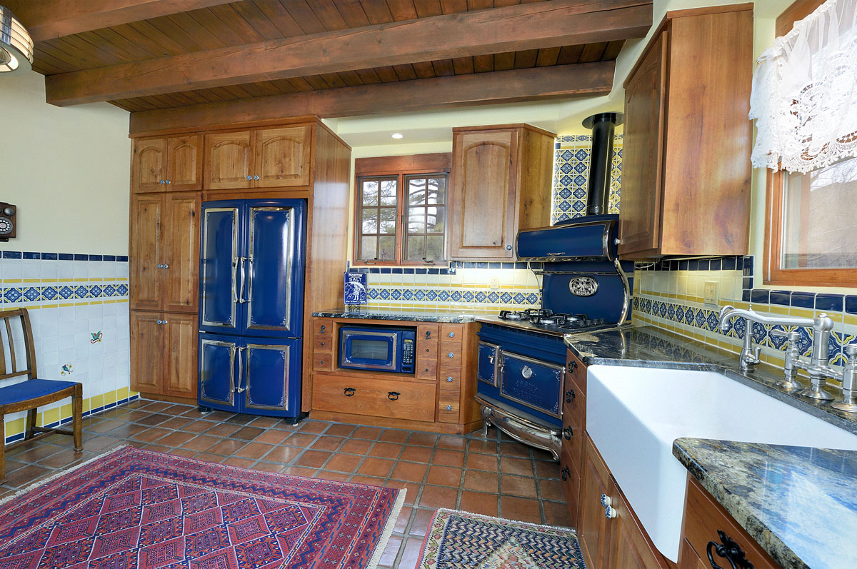 The extended kitchen area exudes vintage elegance with wooden cabinets and navy blue appliances, complemented by hand-painted blue and yellow wall tiles. A strategically placed purple rug adds a pop of color for balanced elegance.