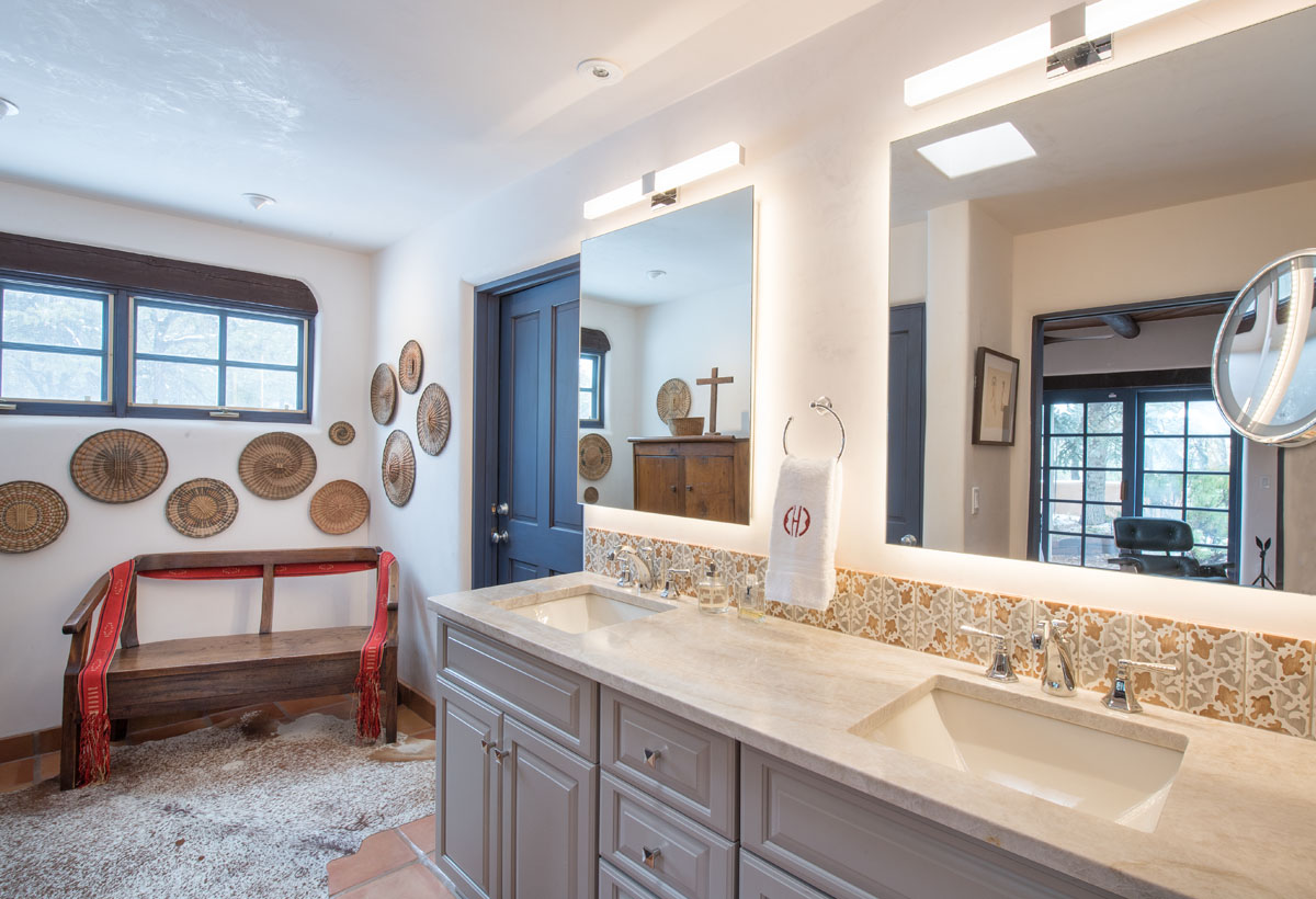 The master bathroom, adorned with ivory white walls, houses a lavatory and cabinets, and features two large mirrors reflecting the serene ambiance. Accents of a blue door and circular mat wall decorations, along with hand-painted and floor tiles, complete the room's refined aesthetic.