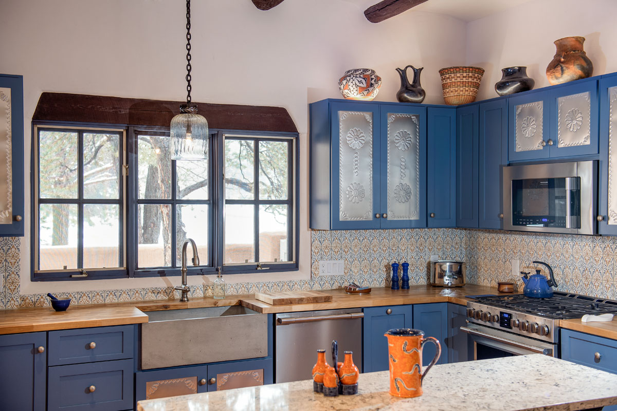 Envision a vibrant kitchen inspired by Southwestern and old Santa Fe themes, with sky-blue cupboards, rustic wooden countertops, walls adorned with white and Saltillo tiles, and natural light streaming through large windows. Dominating the kitchen is a grand granite island, reflecting the hues around and adding to the room's unique character and warmth.