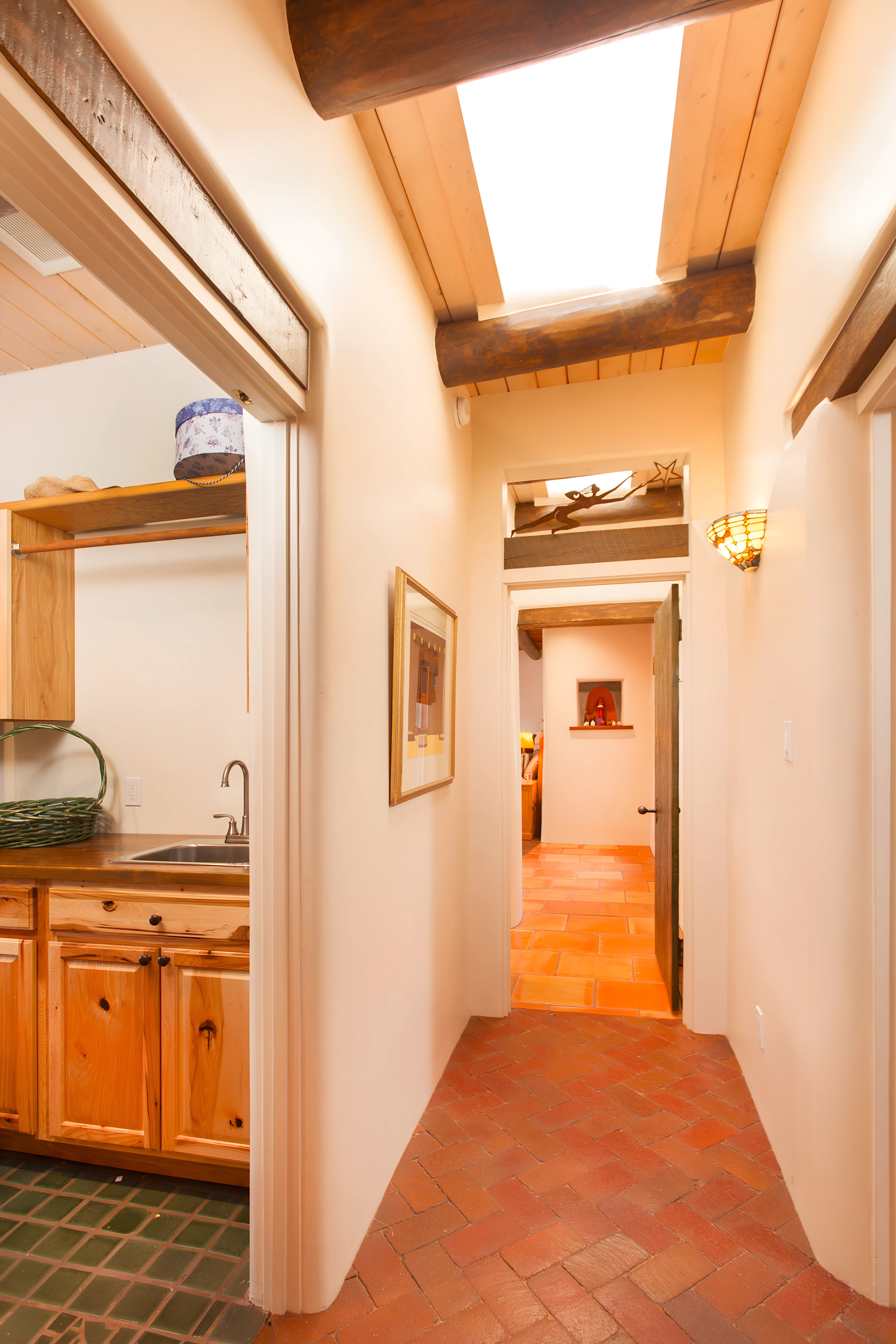 Hallway with rustic wooden beams, terracotta tile flooring, and soft lighting, leading to rooms and an open area with decorative accents.