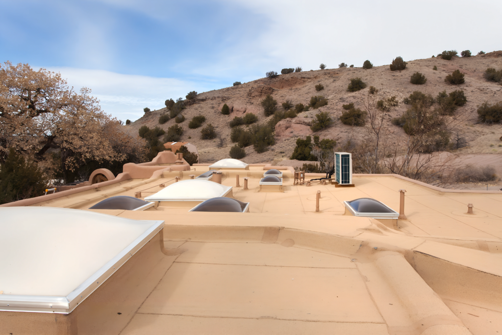 The image shows a flat, sloped roof with several skylights, a solar panel, and a view of the surrounding hilly landscape, giving a clear view of the structure's top features.