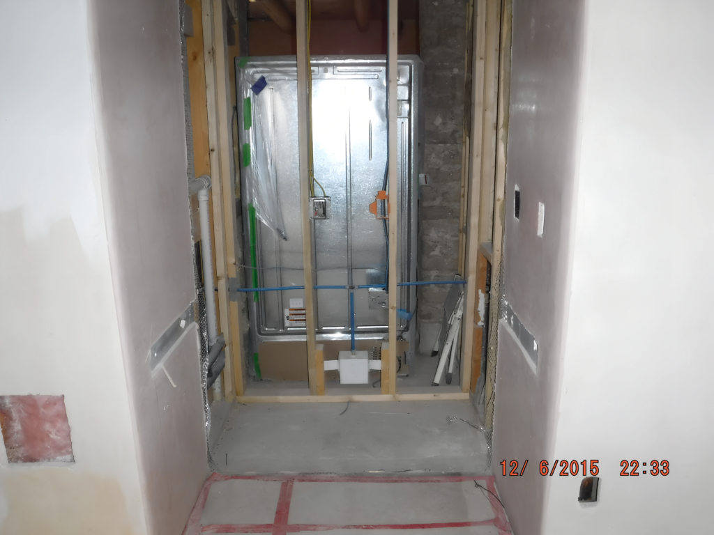 A kitchen space in the middle of renovation, with exposed studs, wiring, and insulation. The framed area is prepped for new appliances, while the walls remain unfinished, signaling ongoing construction and remodeling efforts.