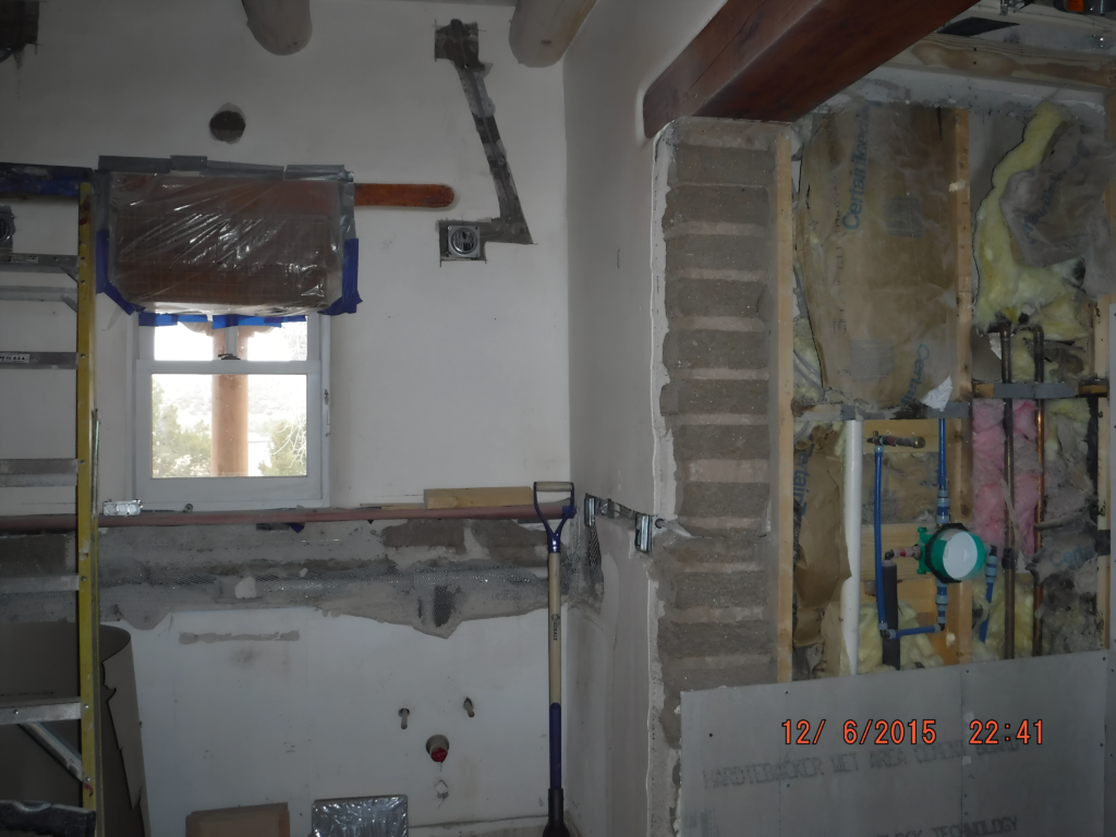 In-progress bathroom renovation with exposed plumbing, insulation, and window. A ladder and construction tools are visible as the room undergoes updates.