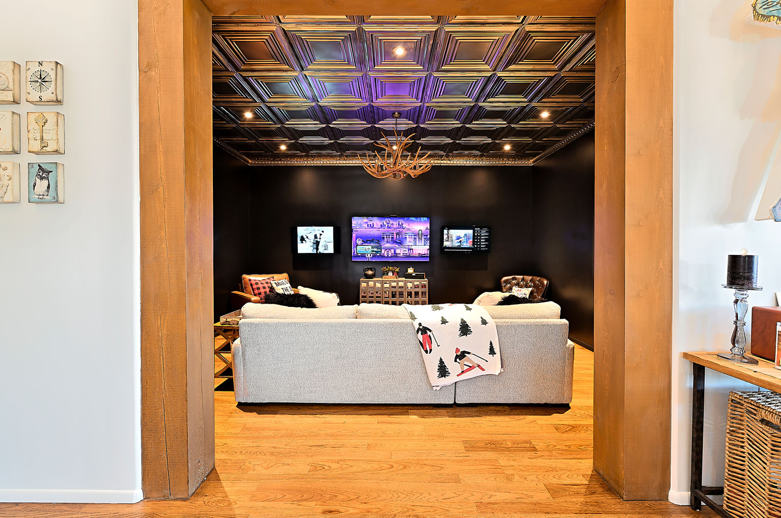 Cozy media room with a vibrant purple ceiling light, dark feature wall, and plush sofa, framed by wooden archways in a Santa Fe home.