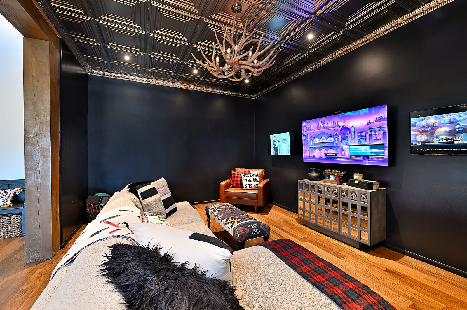 Modern and inviting media room featuring a dark accent wall, stylish antler chandelier, and comfortable seating, perfect for entertainment in a Santa Fe home.