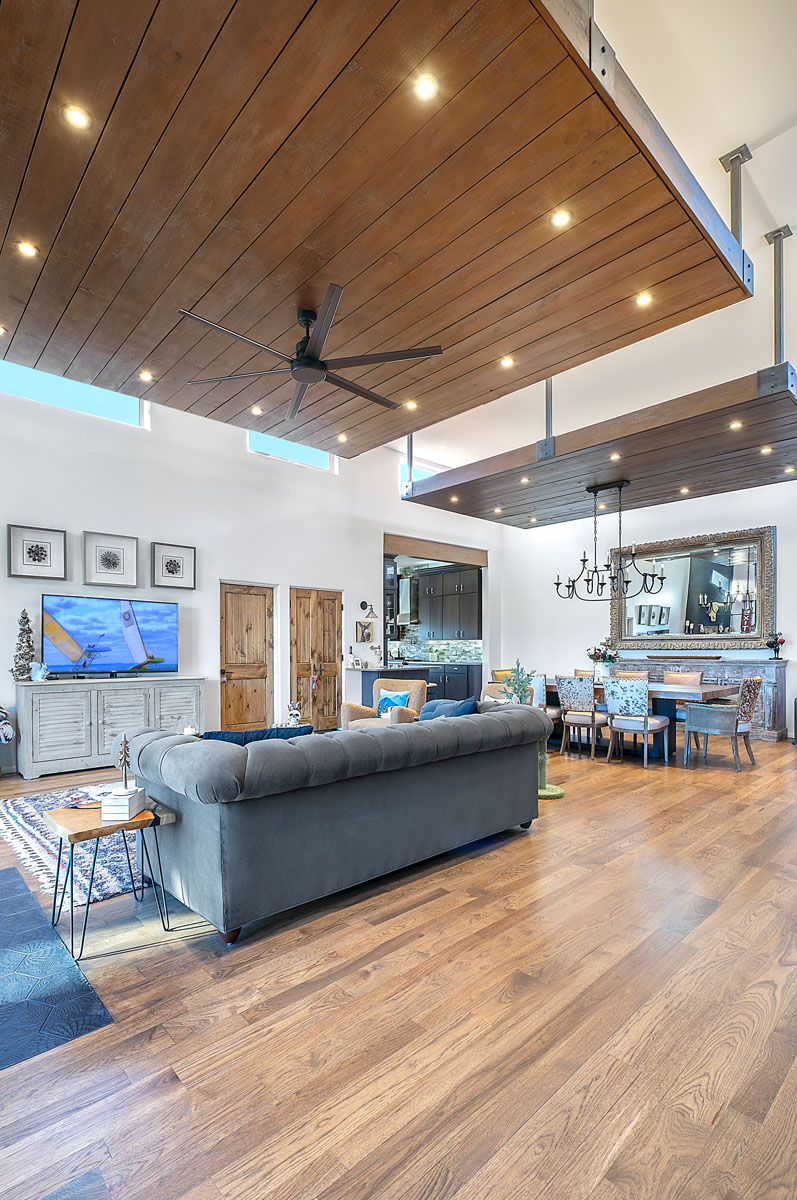Bright and airy living space in a Santa Fe home, featuring wooden ceilings, a large plush sofa, and an open floor plan extending to the dining and kitchen areas.