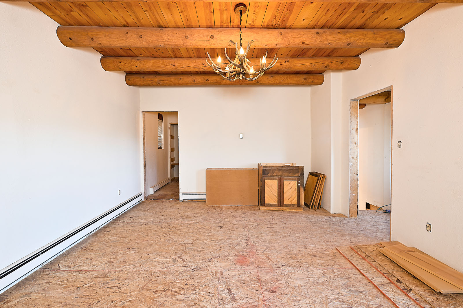 Interior view of a home undergoing remodeling in Santa Fe, showing wooden ceiling beams and an elegant chandelier.