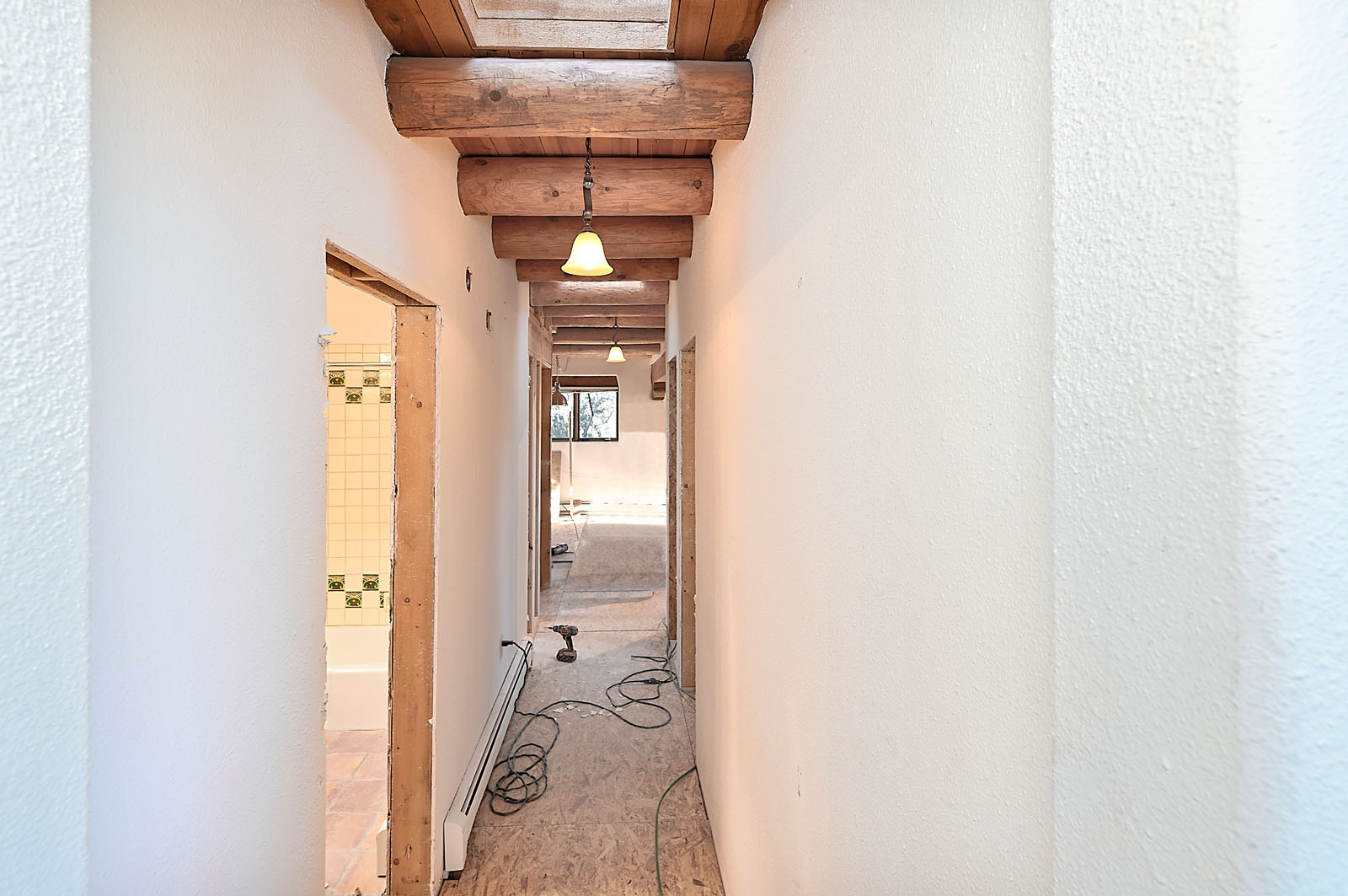 Narrow hallway in a Santa Fe home under renovation, featuring wooden beams and a glimpse into a tiled bathroom.