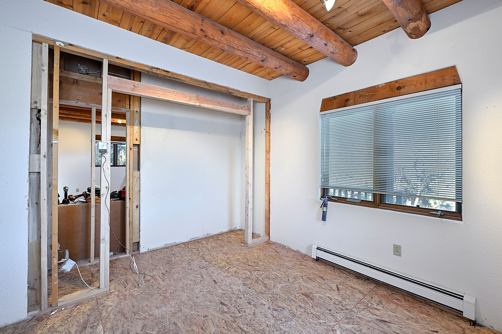 Renovation scene of a room with wooden ceiling beams and an exposed wall, showing in-progress electrical and plumbing works.