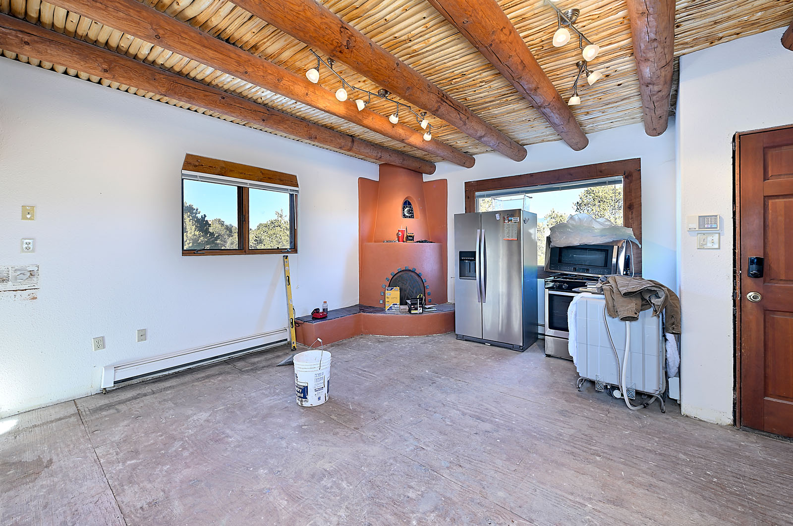 Spacious room under renovation in a Santa Fe home featuring exposed wooden beams, adobe-style fireplace, and scenic window views.