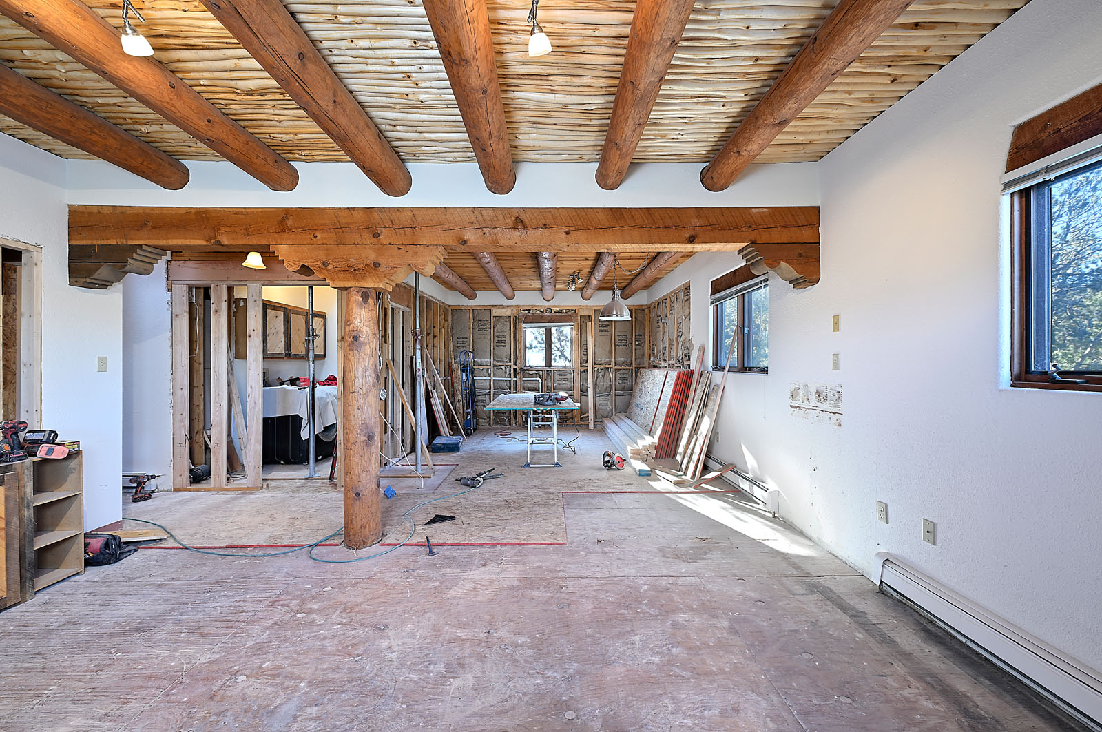 Extensive renovation of a large room in a Santa Fe home, featuring exposed ceiling beams, unfinished walls, and construction materials.