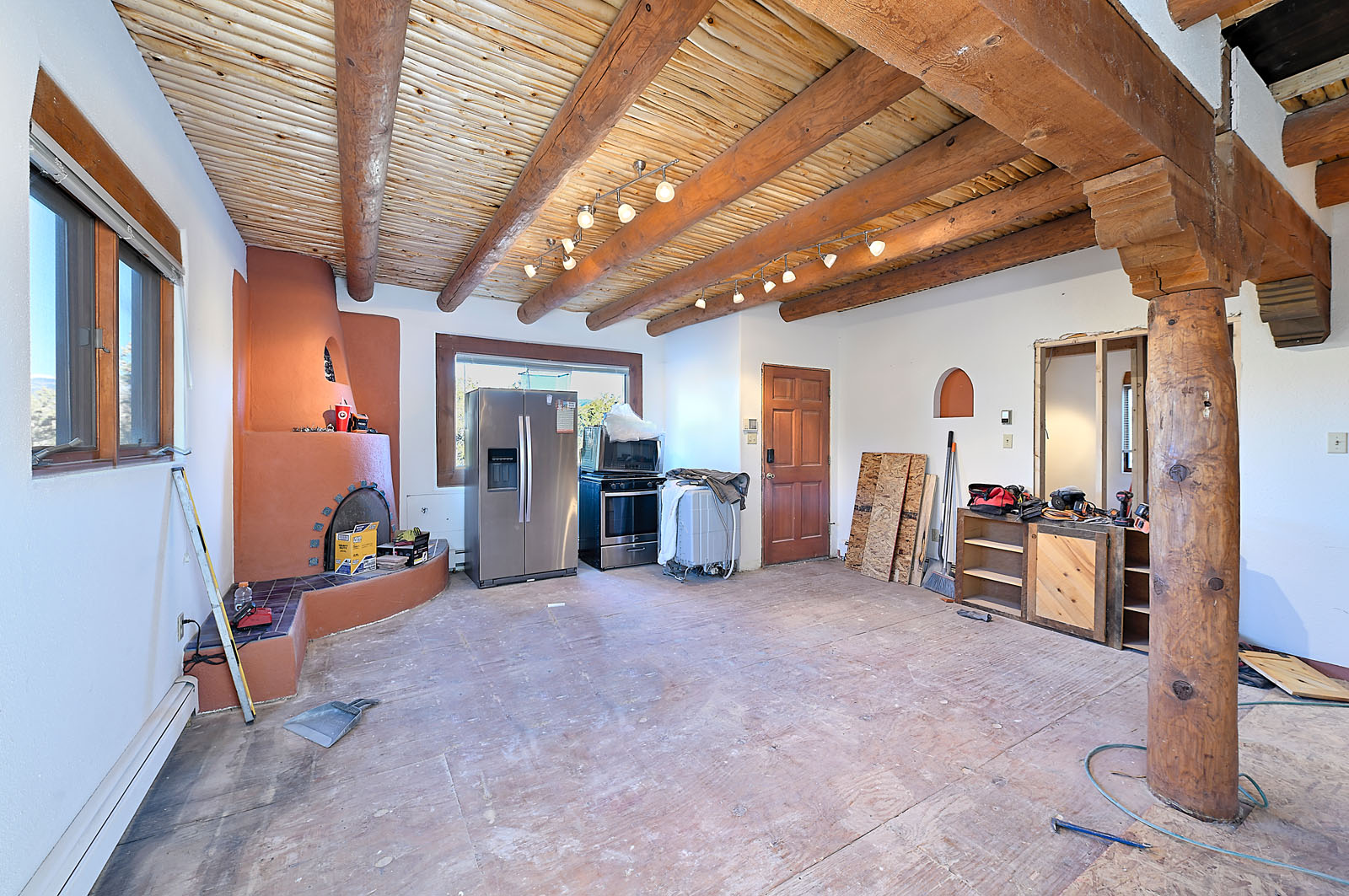 Renovation of a spacious Santa Fe home showcasing exposed wooden beams, adobe walls, and construction equipment scattered throughout the area.