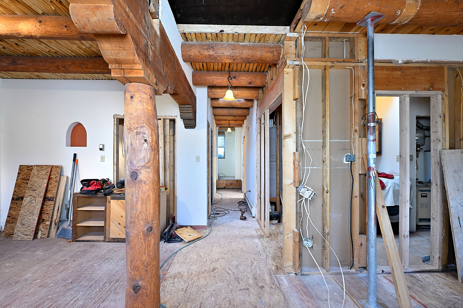 Interior view of ongoing construction in a historic Santa Fe home, featuring rustic wooden columns and exposed ceiling beams.
