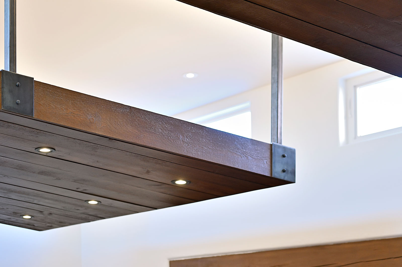 Detail of a modern Santa Fe home showing exposed wooden beams with metal brackets and recessed lighting, highlighting the blend of rustic and contemporary design elements.