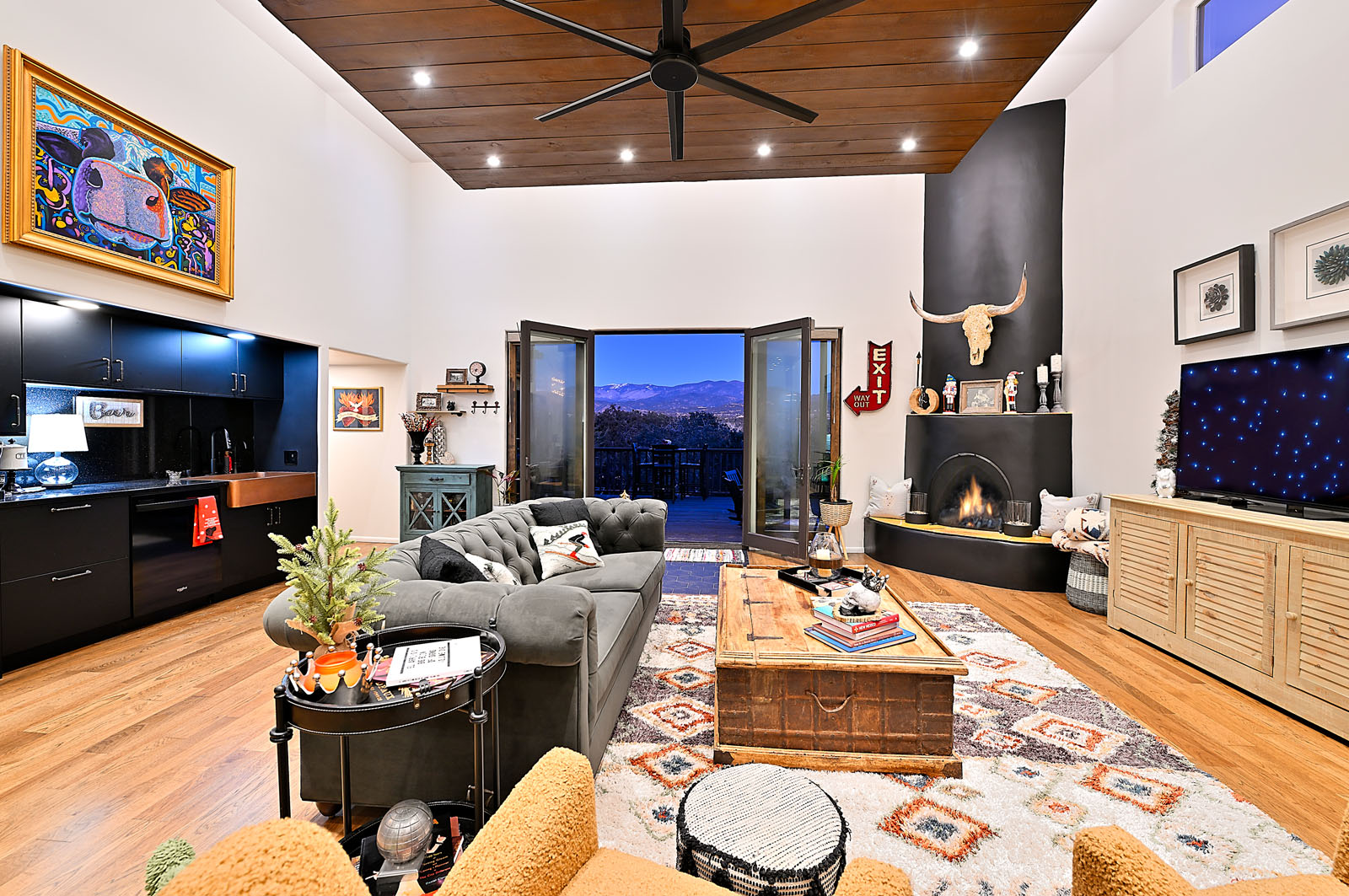 Sophisticated and vibrant living room in a Santa Fe home, featuring a high contrast design with dark walls, colorful artwork, and a panoramic view of the mountains through large doors.
