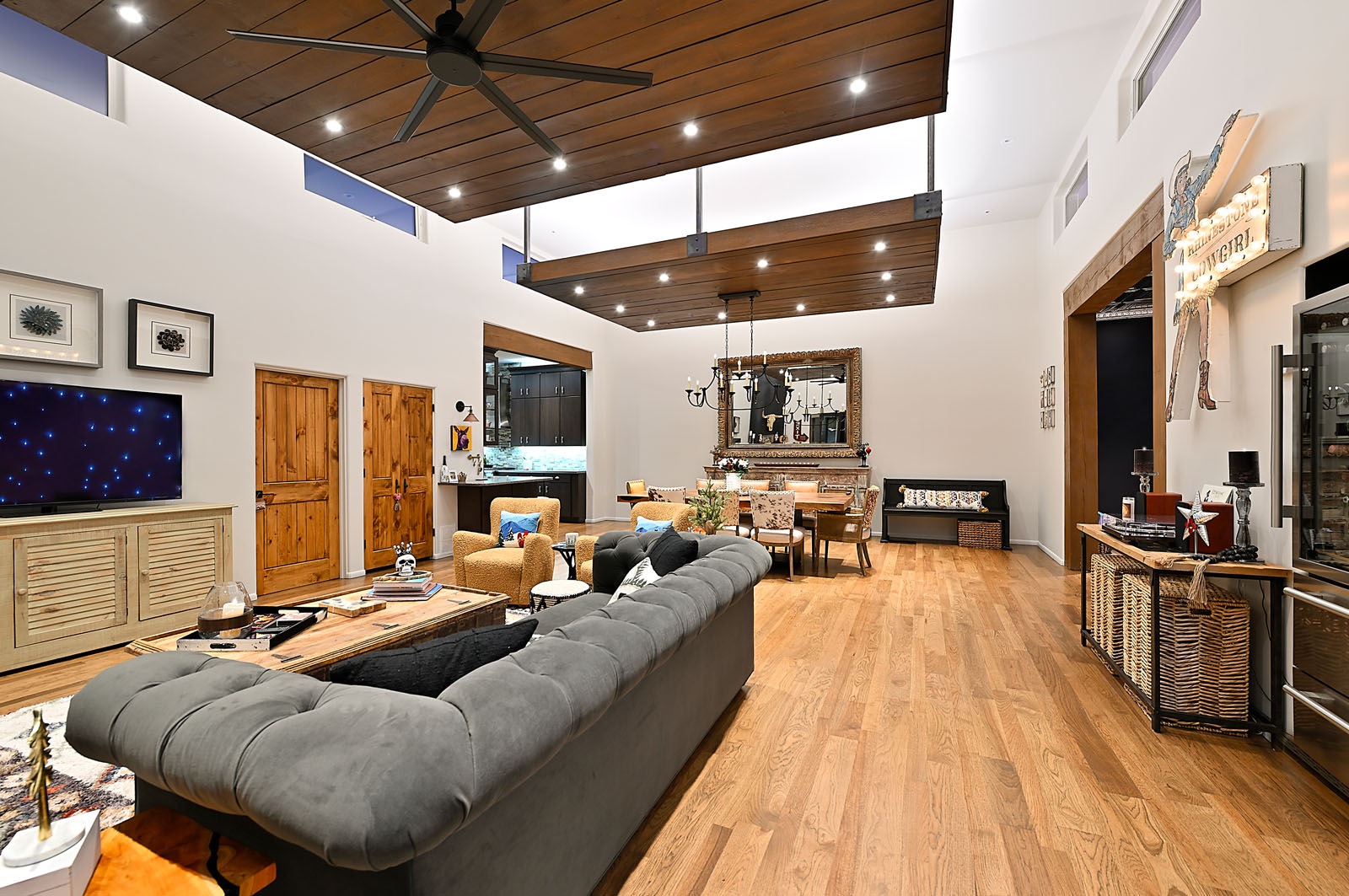 Spacious and luxurious living area in a Santa Fe home featuring high ceilings, hardwood flooring, and a blend of modern and rustic decor, with a view towards the kitchen.